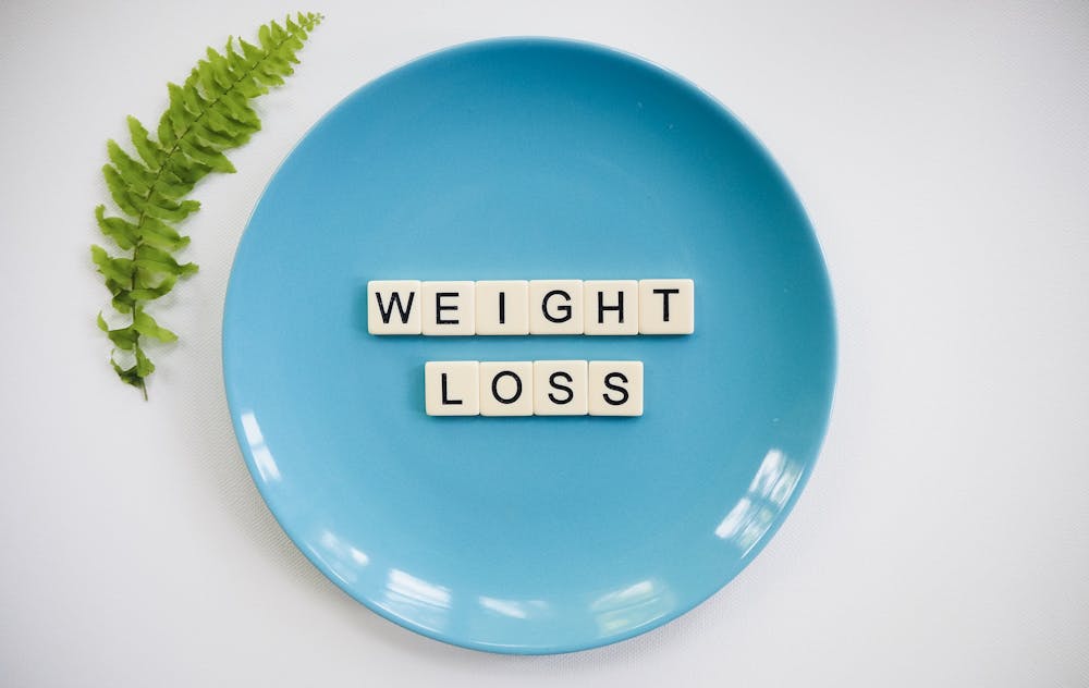 Scientists Create a Promising 4-in-1 Weight Loss Drug A blue plate with 'weight loss' tiles and a fern leaf on white background.