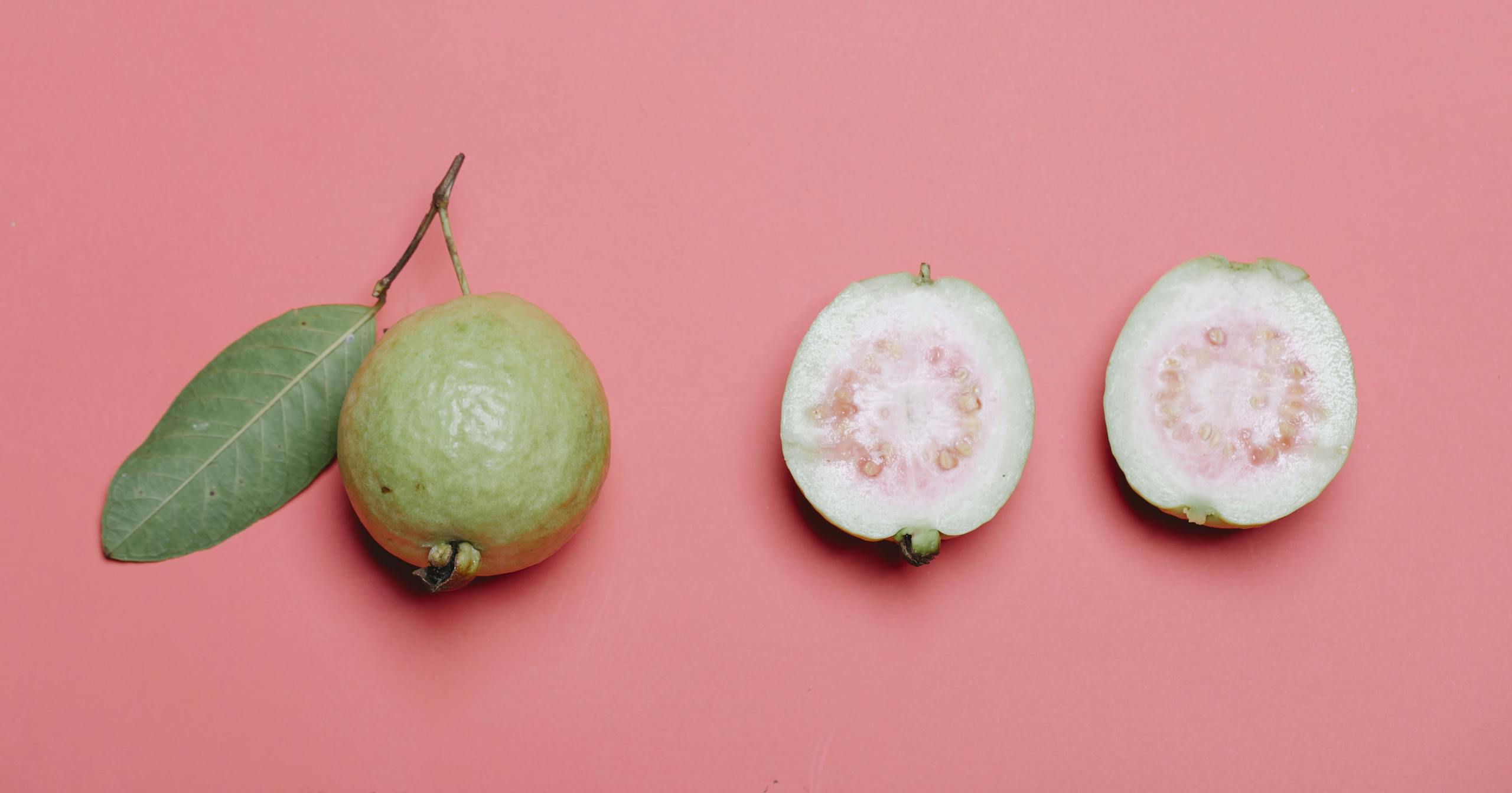A Tropical Fruit Molecule Could Change How We Treat Liver Cancer Whole and cut guava with leaf on pink background. Perfect for healthy eating concepts.