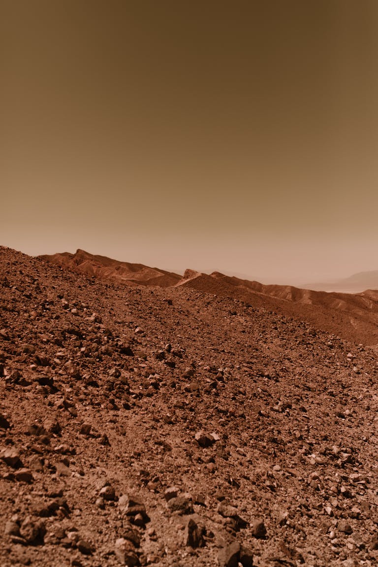 A barren and rocky desert landscape reminiscent of the planet Mars with a warm, dusty sky.