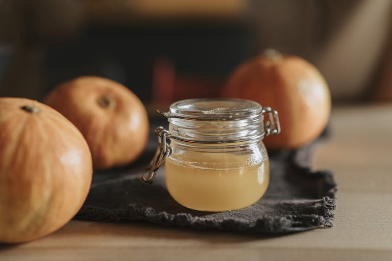A cozy still life with homemade apple cider in a glass jar surrounded by pumpkins on a wooden table.