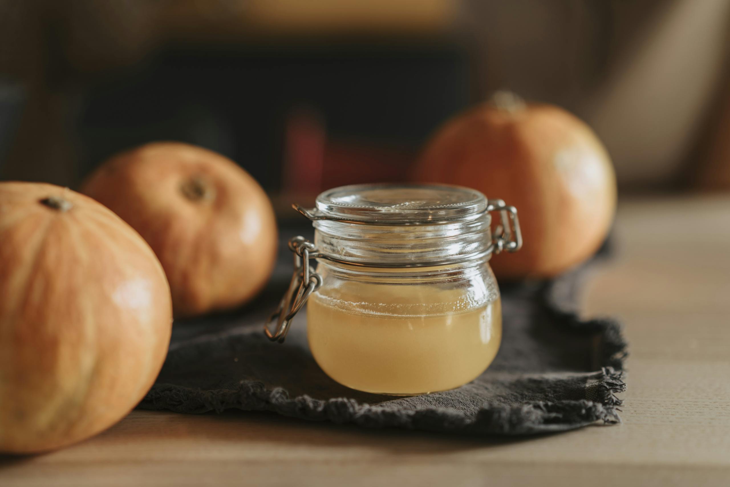 A cozy still life with homemade apple cider in a glass jar surrounded by pumpkins on a wooden table.