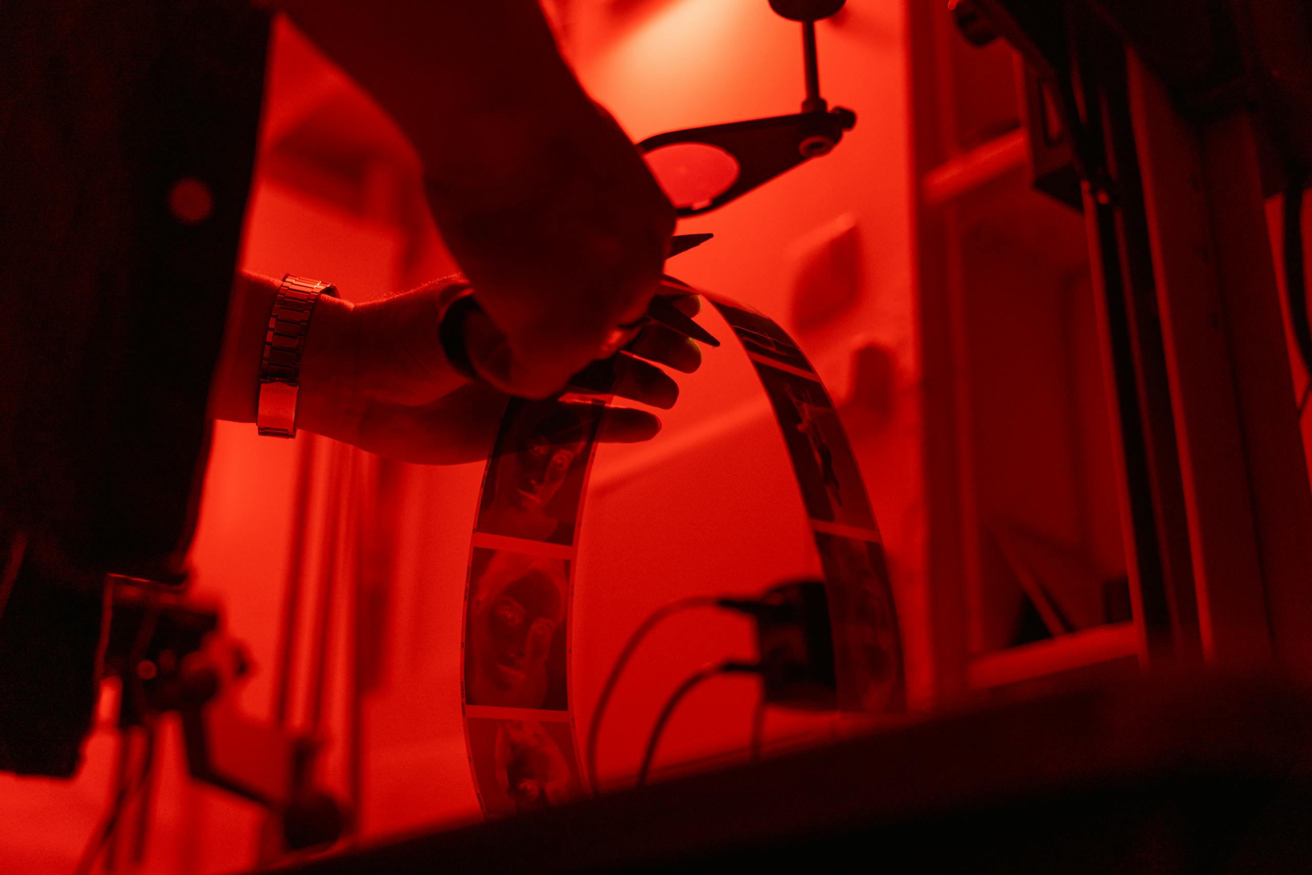 A person works with film negatives in a dimly lit darkroom.