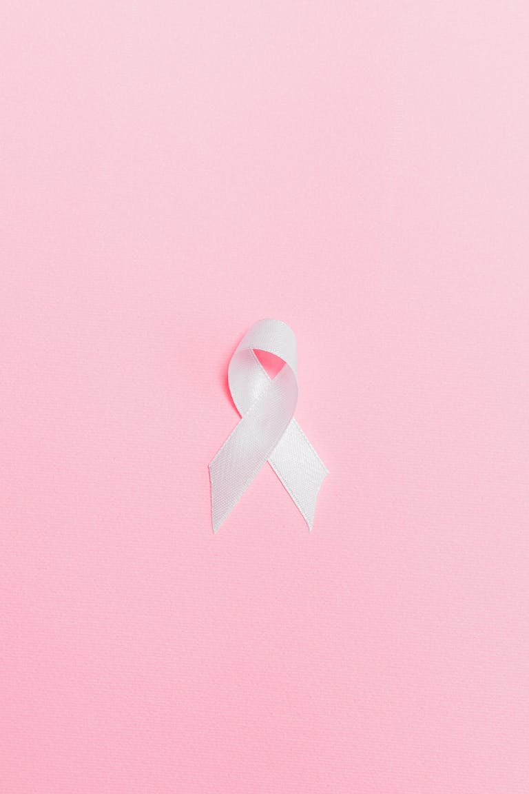 A pink ribbon symbolizing breast cancer awareness set against a light pink background.
