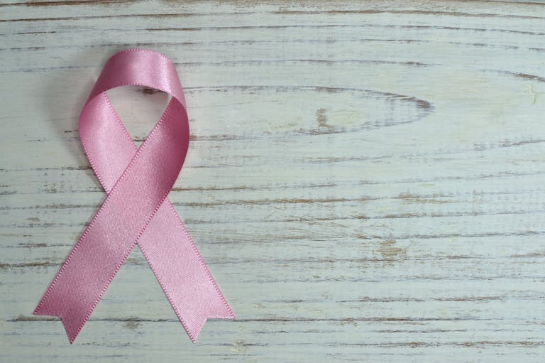 A pink ribbon symbolizing cancer awareness placed on a light wooden background.