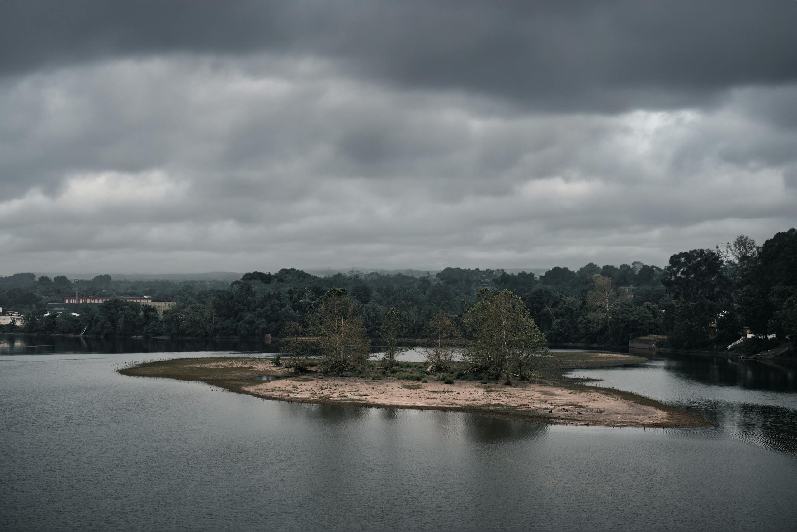A serene river scene with an island and moody overcast clouds, perfect for nature enthusiasts.