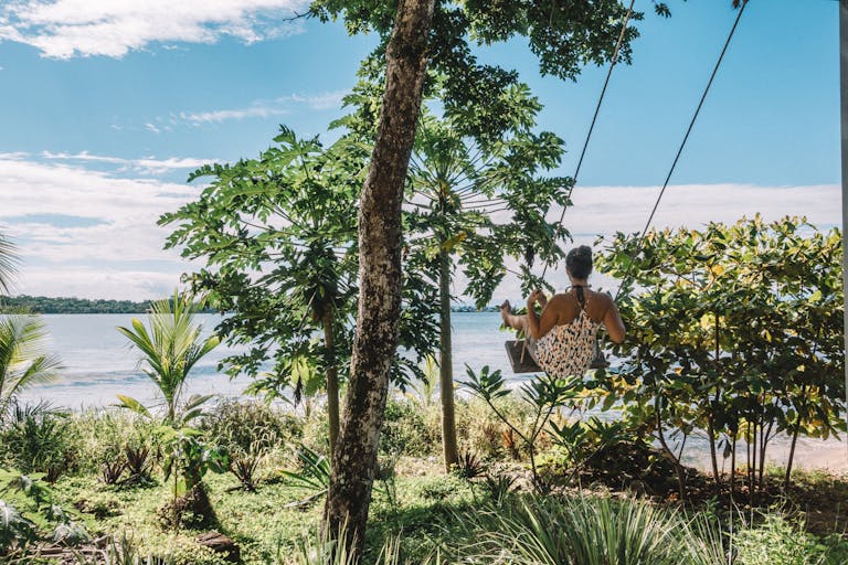 A woman enjoys a swing by the beach, surrounded by lush tropical greenery, capturing the essence of tranquility in Panama.