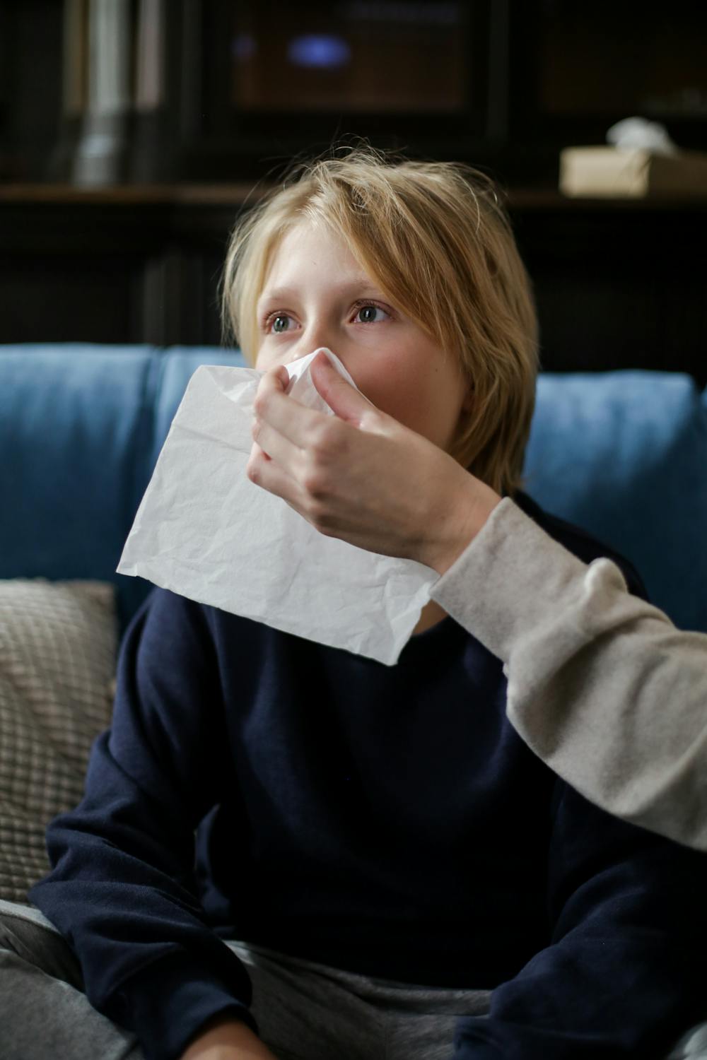 Can the Common Cold Really Help Kids Resist COVID? A young child holding a tissue, assisted by an adult, for sneezing or illness recovery indoors.