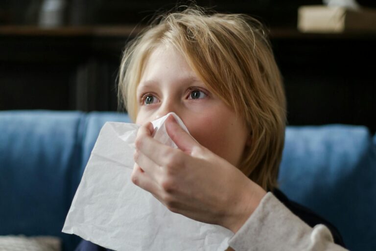 A young child holding a tissue, assisted by an adult, for sneezing or illness recovery indoors.