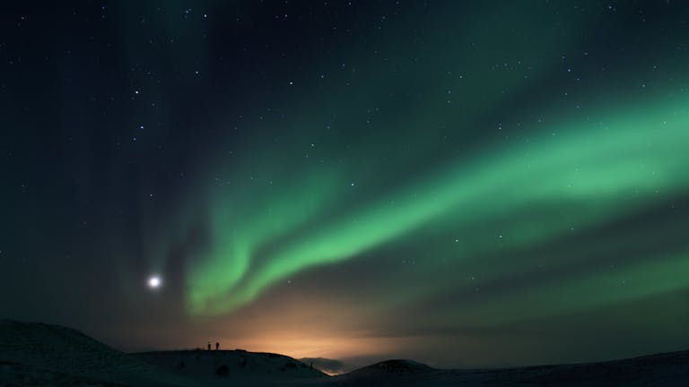 Captivating view of the Aurora Borealis dancing over a tranquil snowy landscape at night.