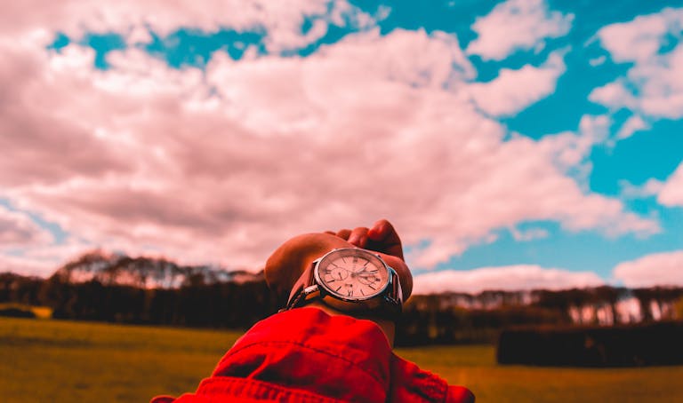 Close-up of a wristwatch with a scenic background of a field and cloudy sky.