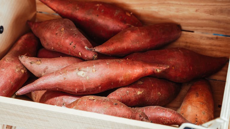 Close-up of fresh sweet potatoes in a wooden crate, ideal for cooking.