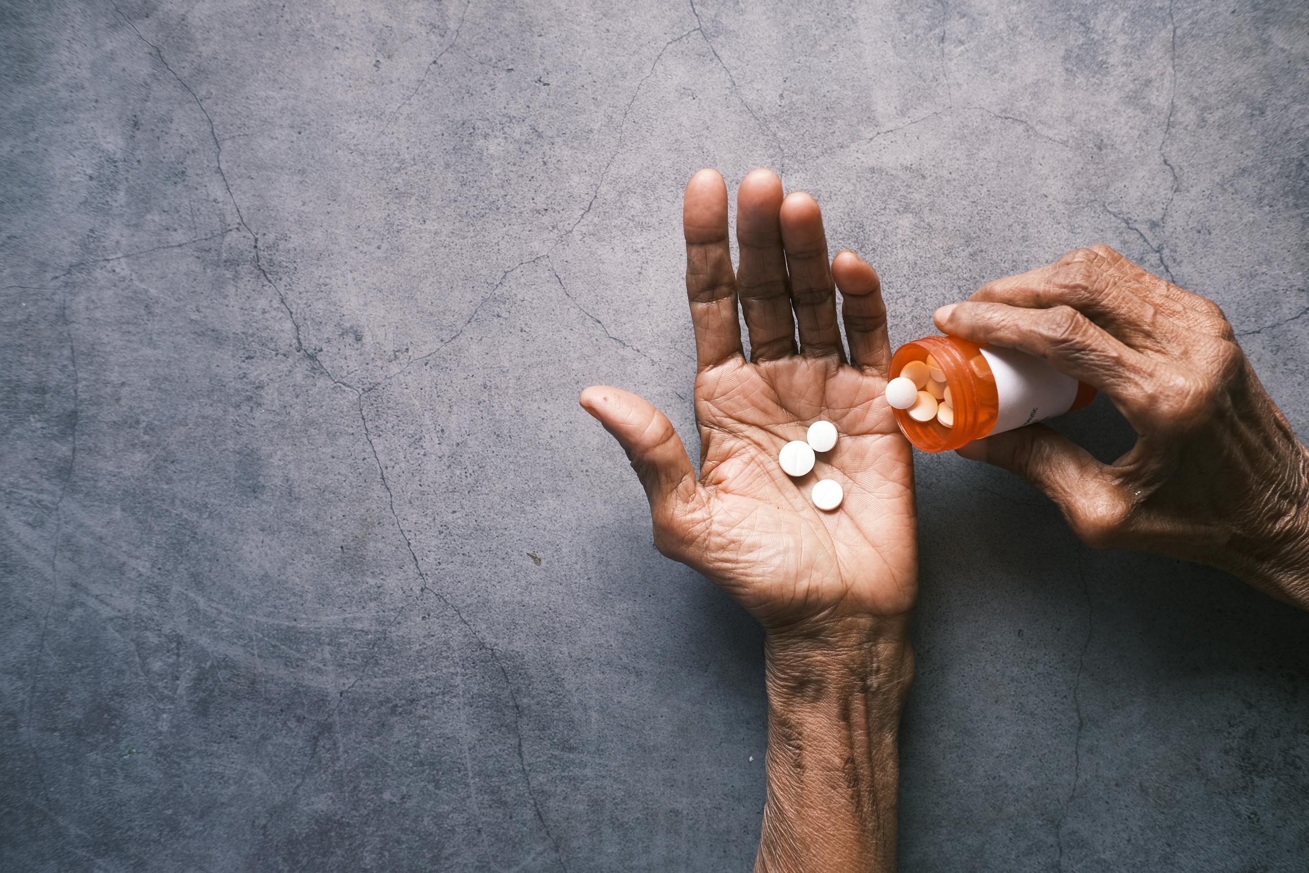 Elderly person's hand pouring pills from a bottle, offering ample copy space.
