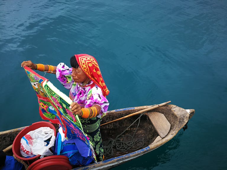 Guna Yala woman in a handcrafted canoe holding colorful textiles in Panama.