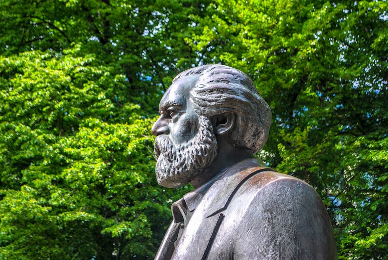 Side view of Karl Marx statue in a lush green Berlin park.