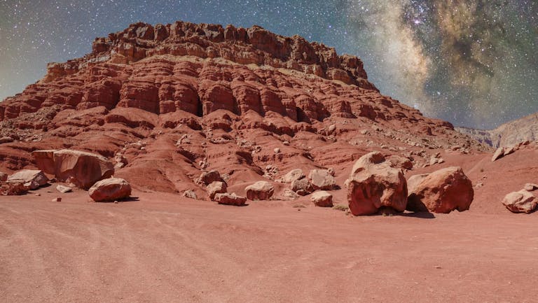 Stunning red rock formations under the Milky Way, resembling a Martian terrain.