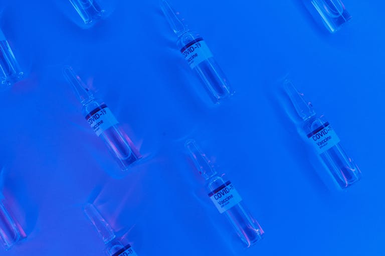 Top view of COVID-19 vaccine vials set against a bright blue background with a neon effect.