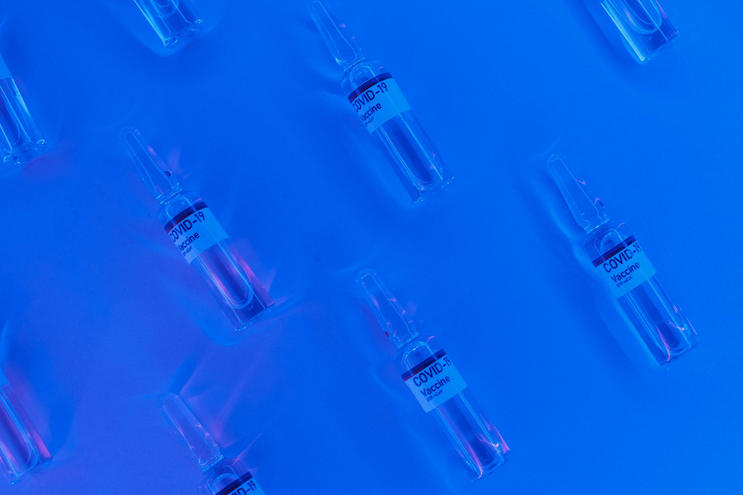 Young Immune Cells Show Promise in Reversing Alzheimer’s and Aging Effects Top view of COVID-19 vaccine vials set against a bright blue background with a neon effect.
