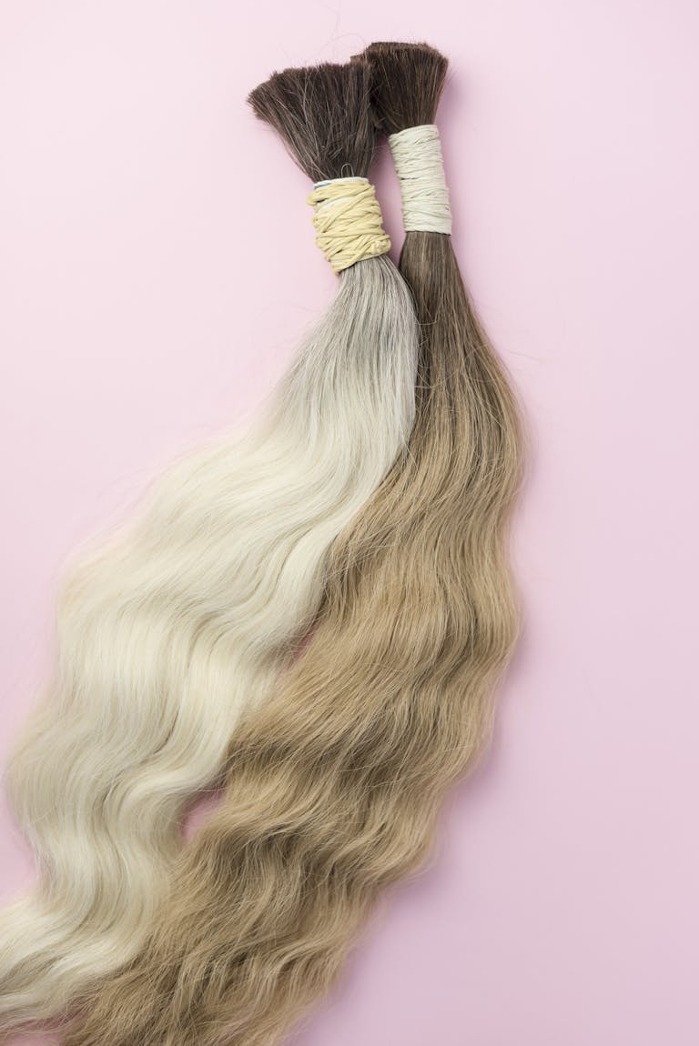 Two elegant hair extensions in contrasting colors on a soft pink backdrop.