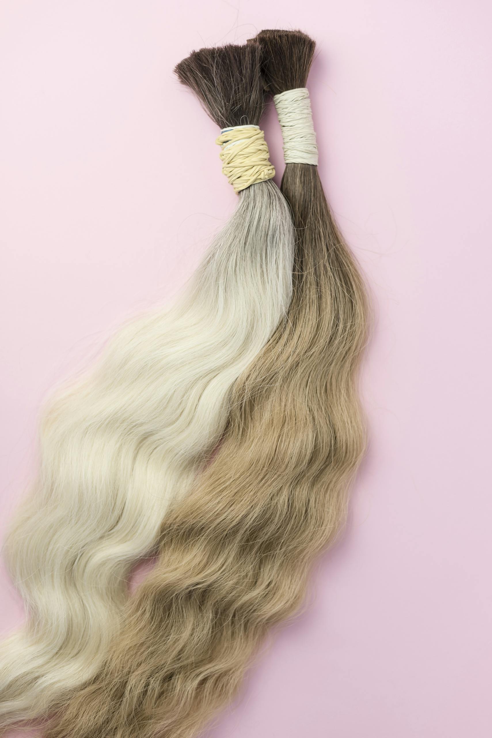 Two elegant hair extensions in contrasting colors on a soft pink backdrop.