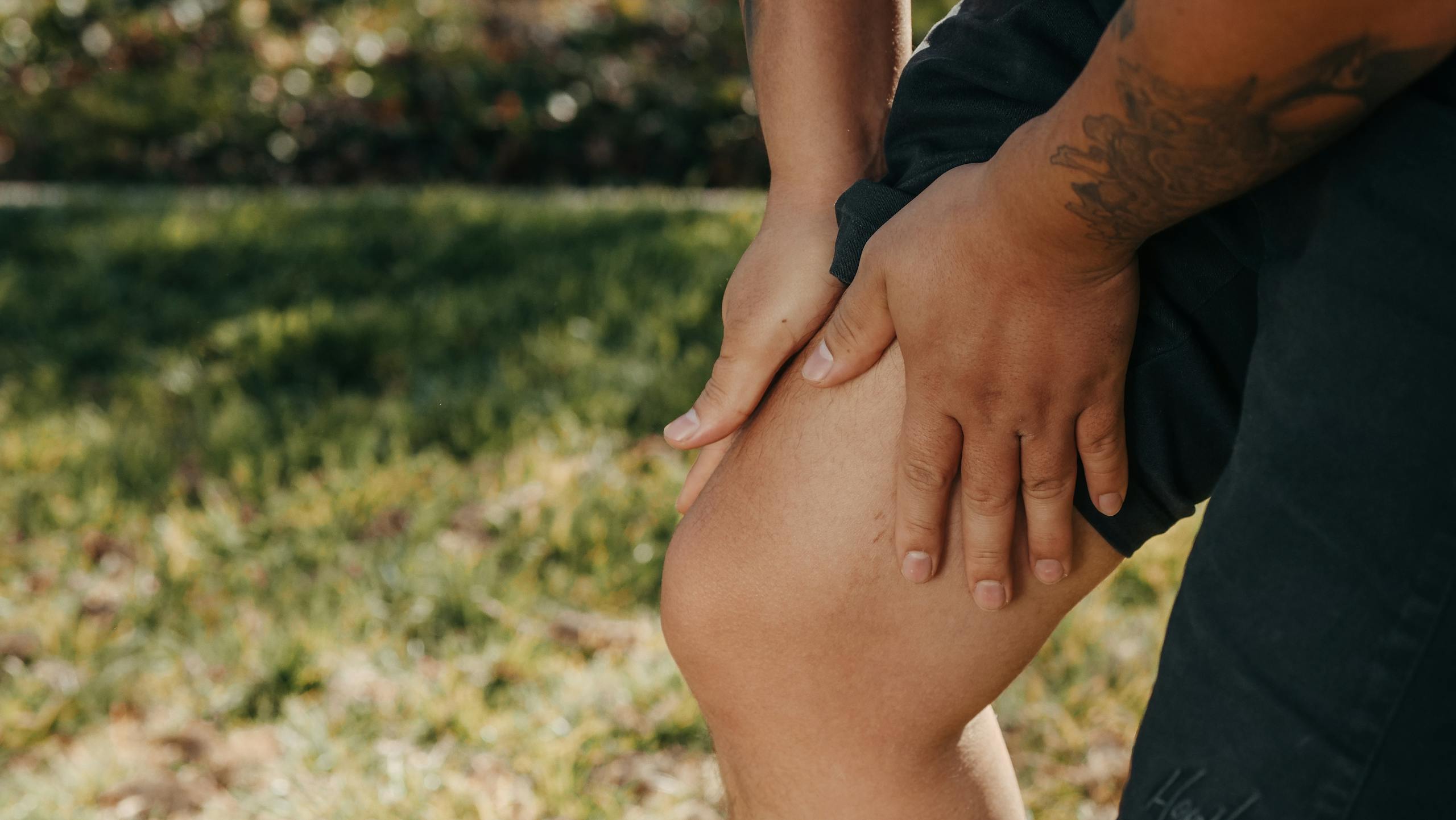 Low-Dose Radiation Therapy Shows Real Promise for Easing Knee Osteoarthritis Pain Without Surgery A close-up image of a person holding their knee, indicating pain or injury, with greenery in the background.