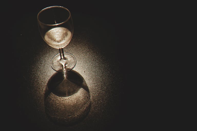 A crystal wine glass casting shadows with light reflections on a dark surface.