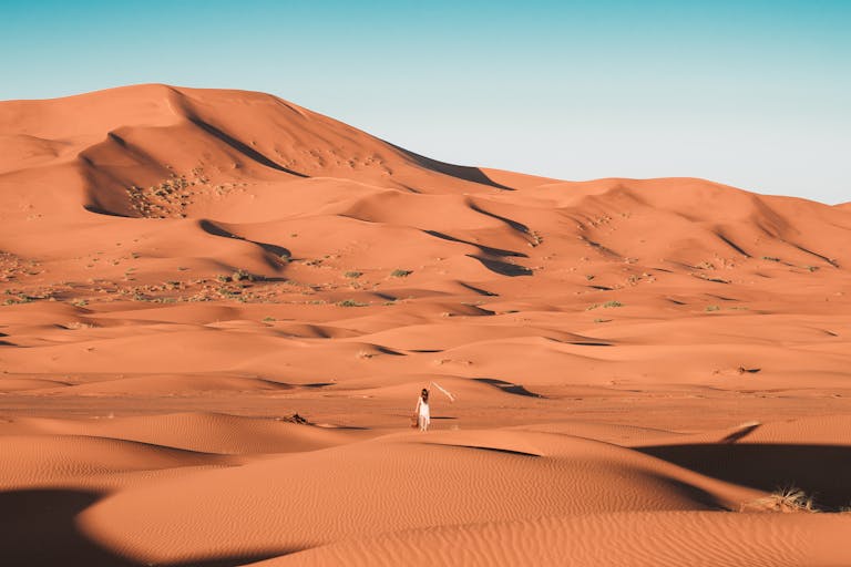 Rain in the Sahara? Scientists Predict a Wetter Future for Africaโs Largest Desert A lone person walking amidst the vast sand dunes of the Sahara Desert under a clear blue sky.