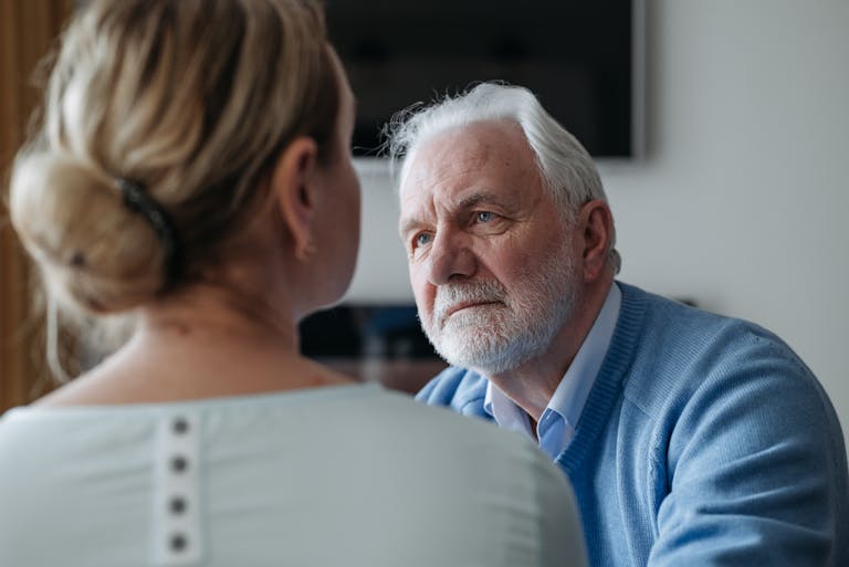 A thoughtful elderly man with grey hair having a conversation indoors, focused on a woman.