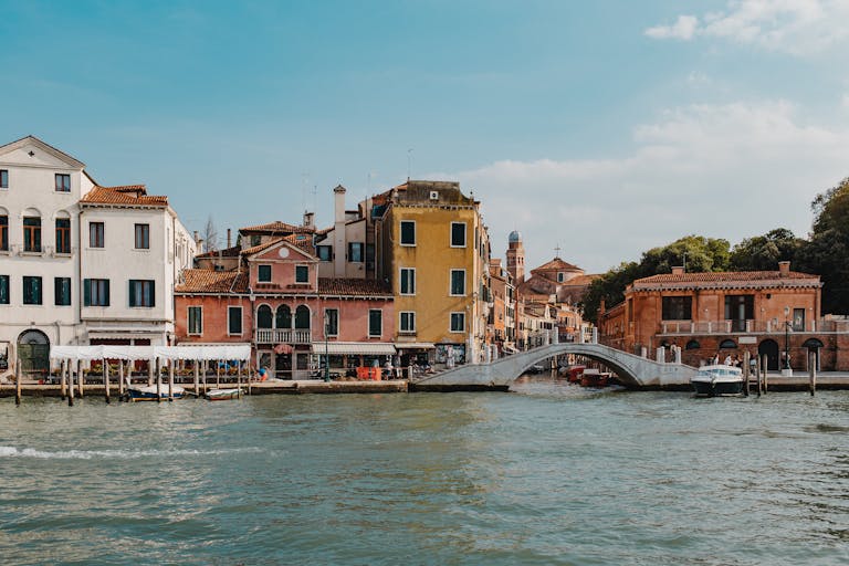 Emission Cuts Before Mid-Century Could Prevent 0.6 Meters of Future Sea-Level Rise Charming view of Venice's canal with vibrant buildings and a stone bridge under a clear sky.