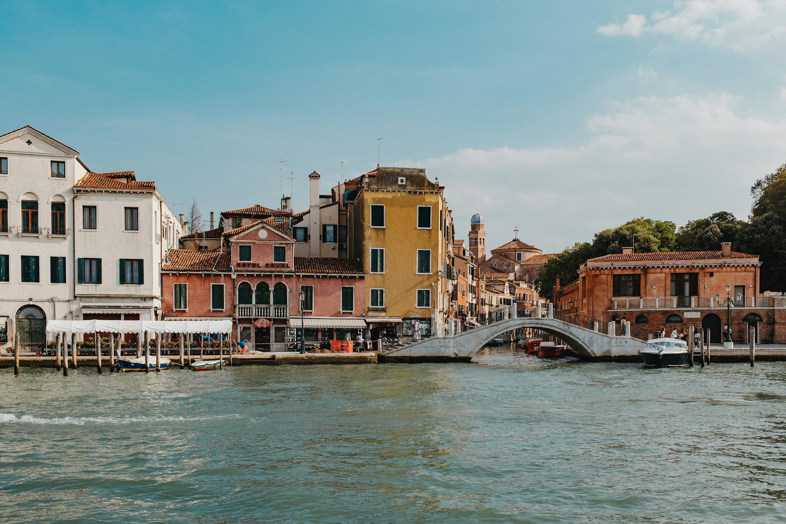 Emission Cuts Before Mid-Century Could Prevent 0.6 Meters of Future Sea-Level Rise Charming view of Venice's canal with vibrant buildings and a stone bridge under a clear sky.