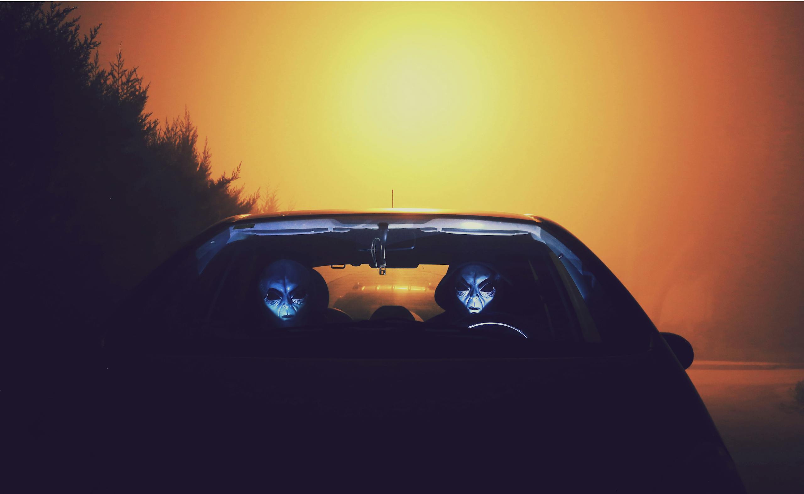 Alien Civilizations Might Be Detectable Only for a Cosmic Blink of an Eye Eerie alien figures with masks seen driving a car during a colorful sunset.