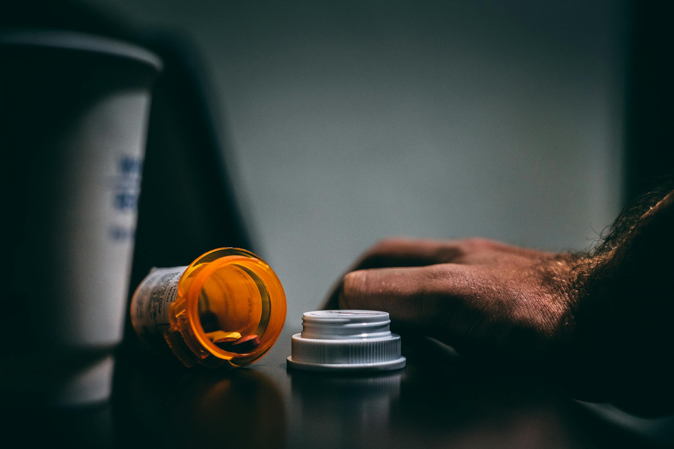 A 9,000% Surge in Fentanyl-Stimulant Deaths Among Seniors: The Fourth Wave of the Opioid Crisis Moodily lit scene of an open prescription bottle and hand on a table, depicting healthcare themes.