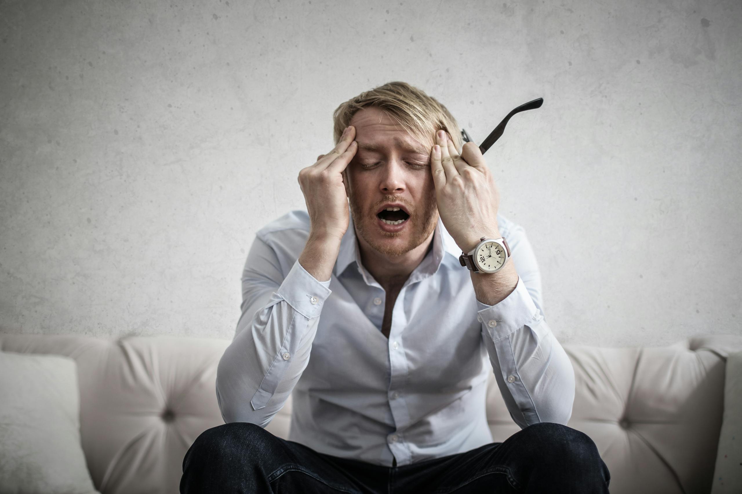Memory Troubles on the Rise: Cognitive Difficulties Nearly Double Among Young Adults in the U.S. Stressed man sitting on couch, feeling overwhelmed and frustrated, expressing mental strain.