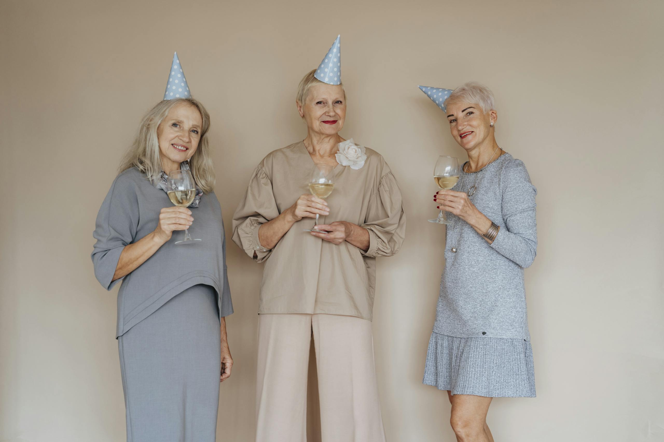 Landmark Study Warns: Average Lifespans May Never Reach 100 Again Three joyful senior women in party hats with glasses of wine celebrating indoors.