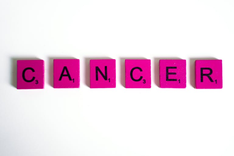 Word 'cancer' spelled with pink letter tiles on a white background symbolizing awareness.