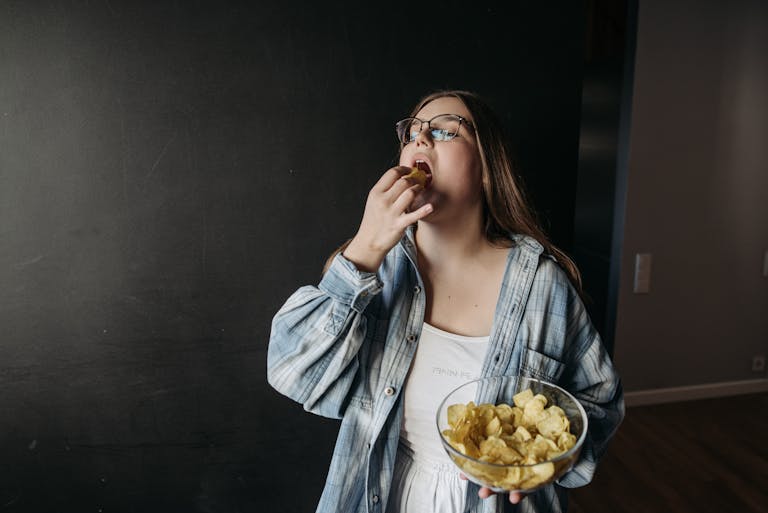 Young woman eating potato chips indoors, enjoying a snack moment.
