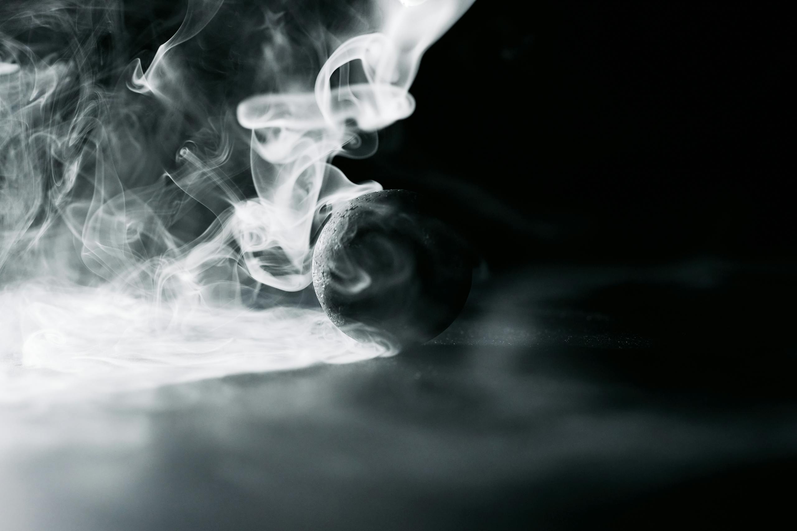 A dramatic black and white image of smoke swirling around a lone sphere, creating a mysterious and artistic effect.