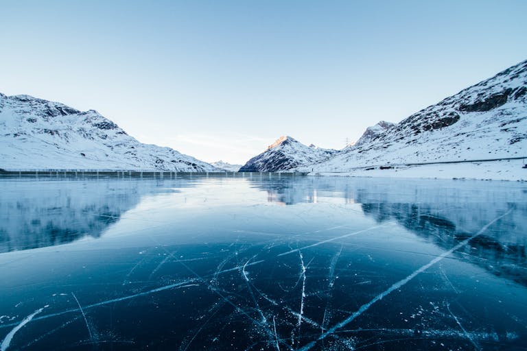 A serene winter landscape featuring a frozen lake surrounded by snow-covered mountains in Switzerland.