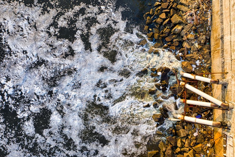 Aerial view of polluted water flowing through pipes into a Jakarta river, causing environmental concerns.