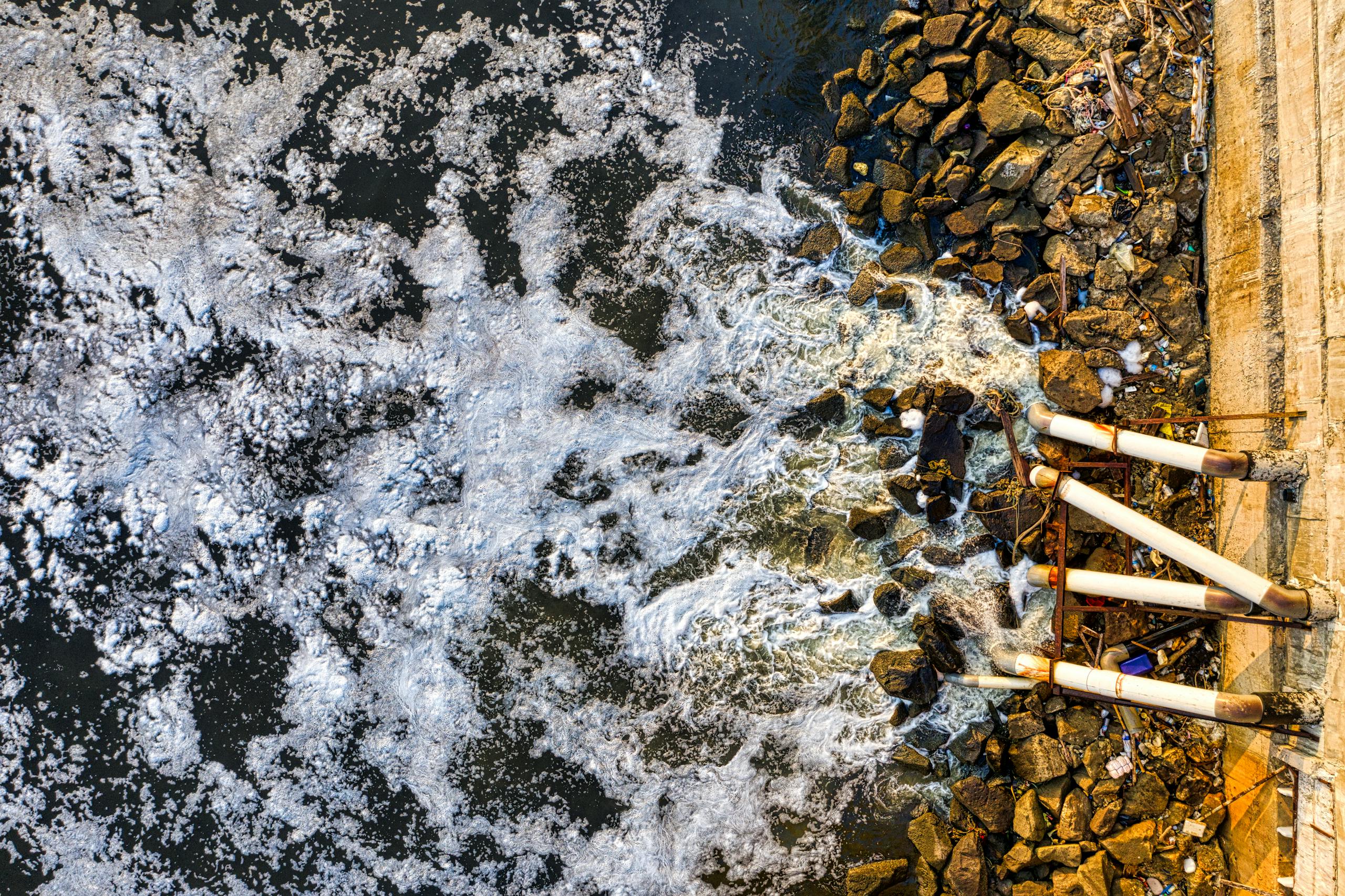 Aerial view of polluted water flowing through pipes into a Jakarta river, causing environmental concerns.