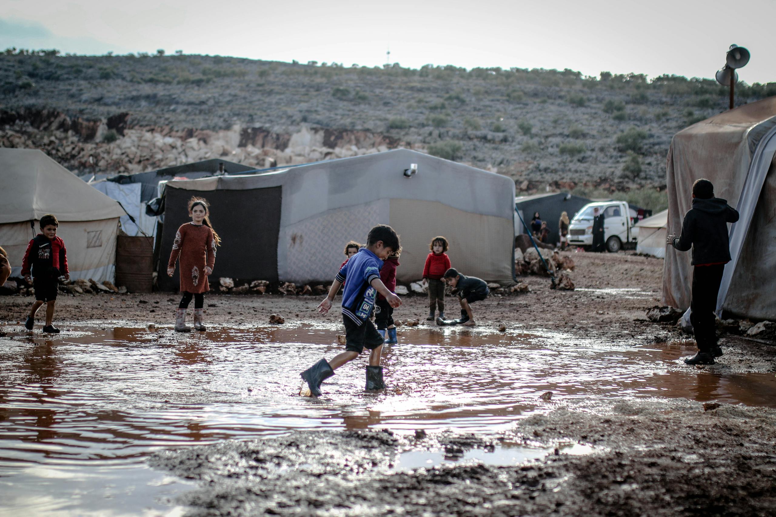 Children play in a muddy area within a refugee camp in Idlib, Syria, showcasing resilience amid challenging conditions.