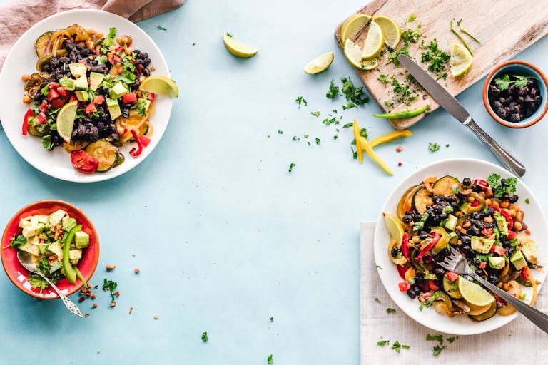 Colorful Mexican salad with avocado, black beans, and lime on a light blue surface.