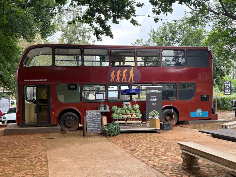 Double-decker bus repurposed as a unique outdoor cafe with fruit display on a sunny day.