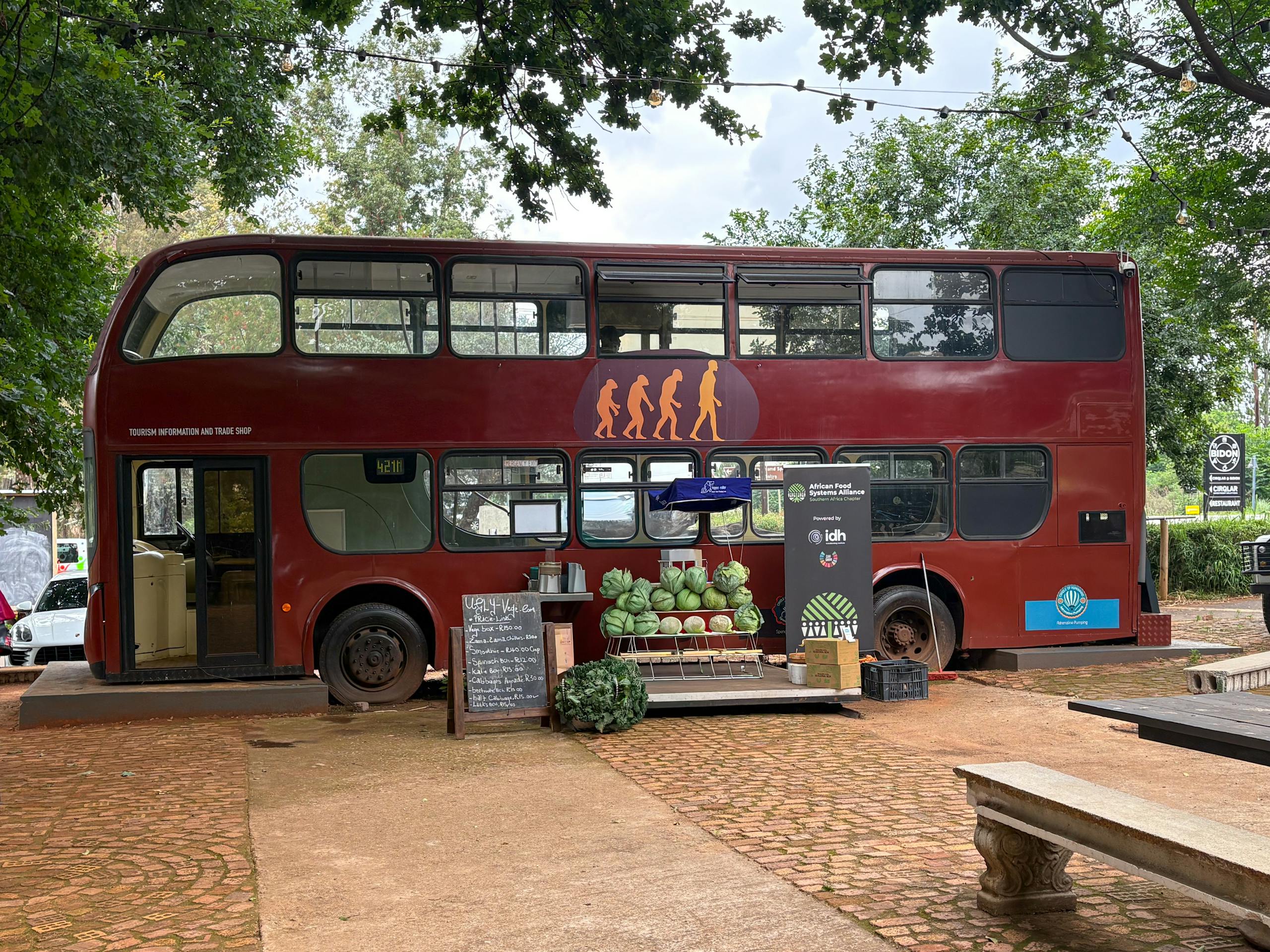 Double-decker bus repurposed as a unique outdoor cafe with fruit display on a sunny day.