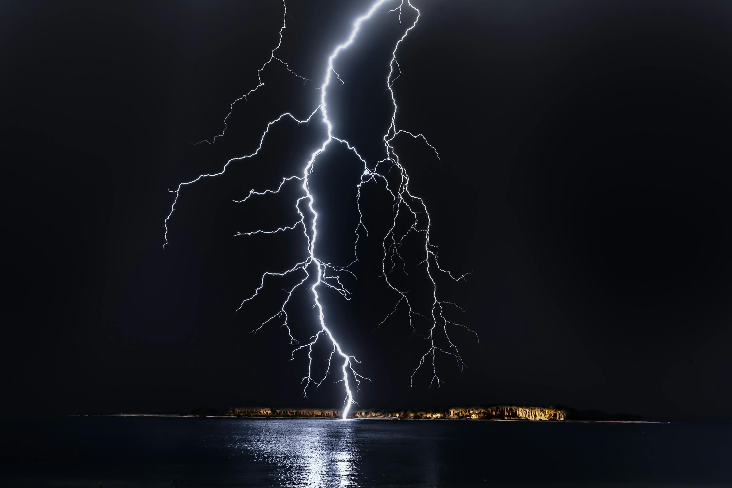 Dramatic lightning bolt over the ocean at night, illuminating the coastal landscape.