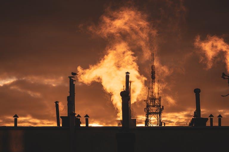 Silhouette of industrial plant smokestacks against a dramatic sunset sky.