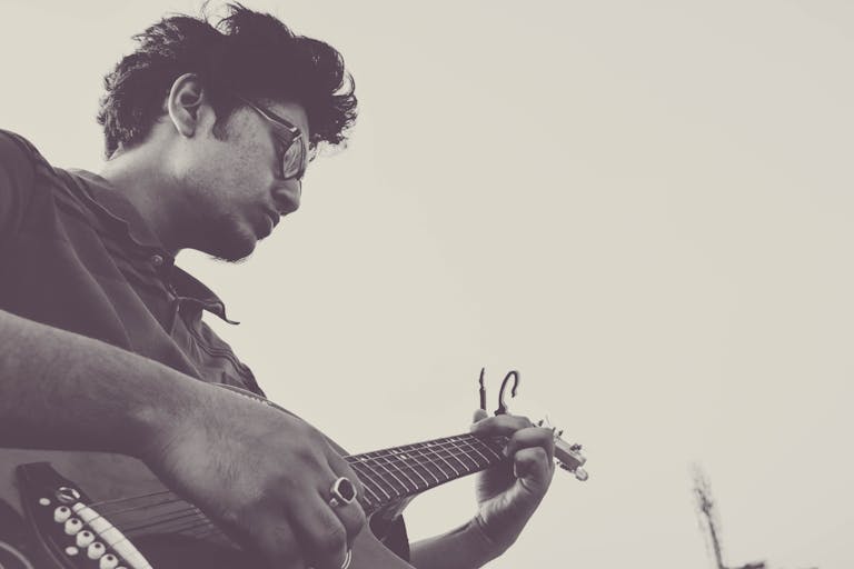 A black and white side view portrait of a male guitarist playing solo outdoors.