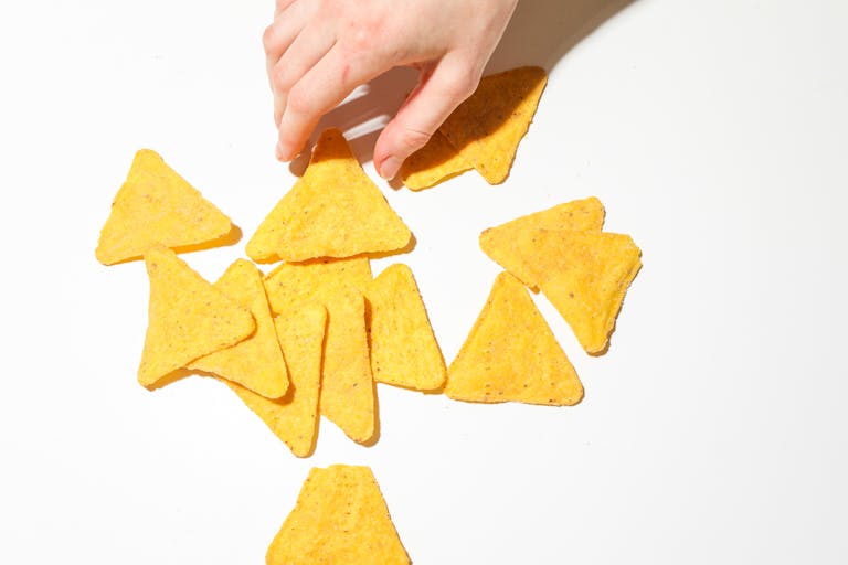 A close-up of a hand grabbing crispy triangular tortilla chips on a white background.