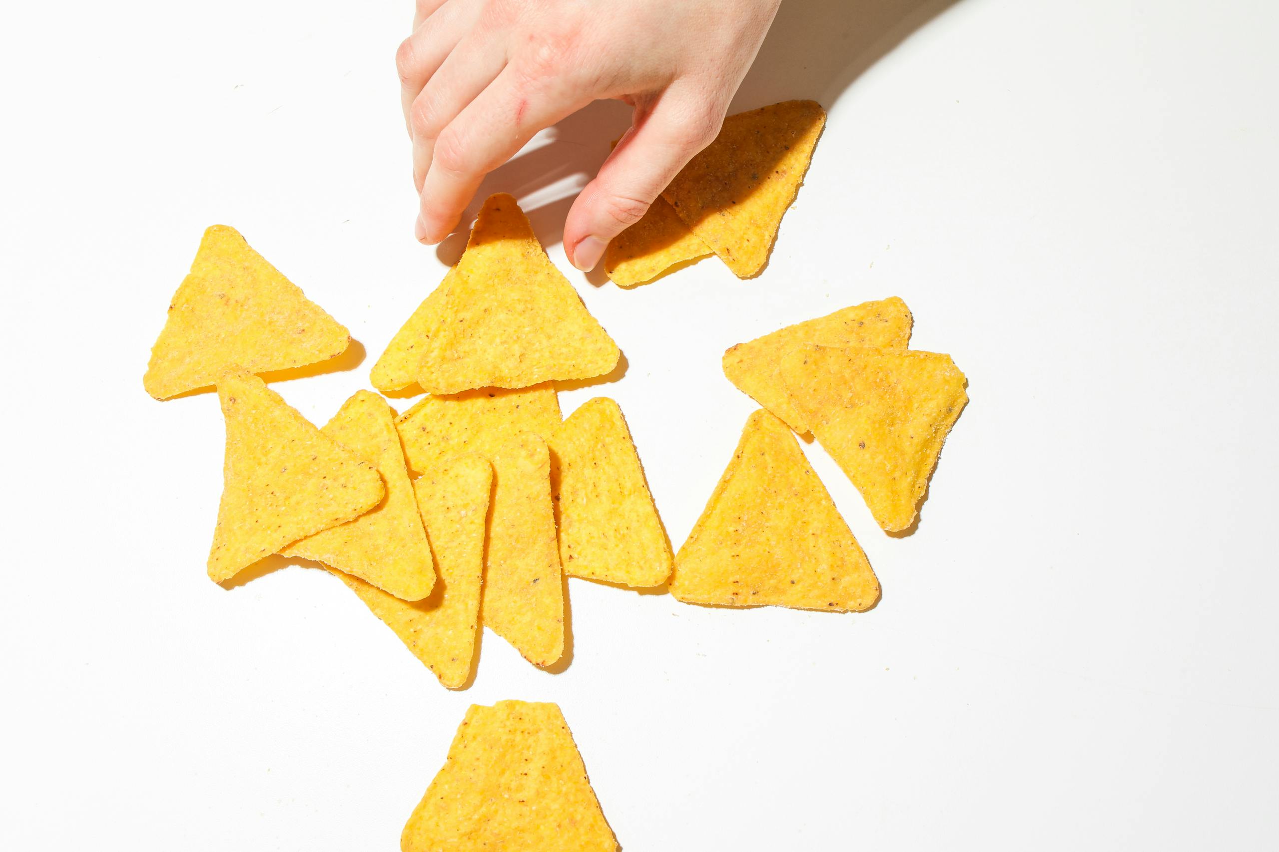A close-up of a hand grabbing crispy triangular tortilla chips on a white background.