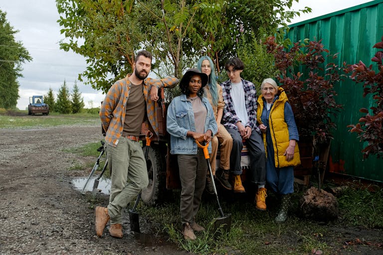 A diverse group of farmers posing with tools and equipment outdoors, showcasing teamwork and agricultural lifestyle.