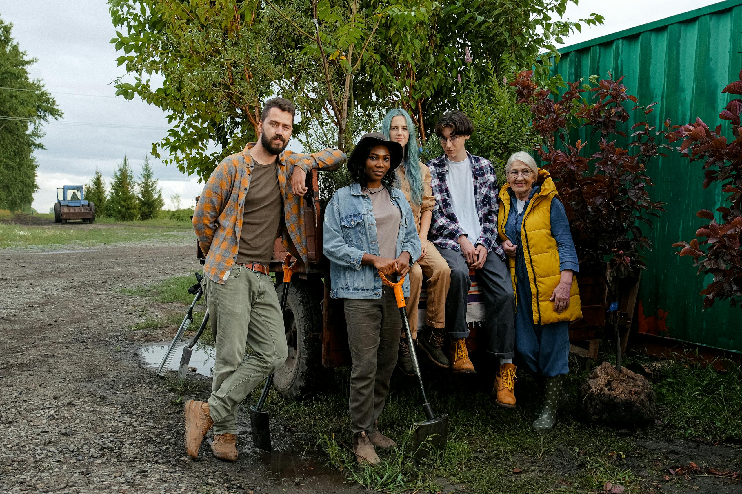 A diverse group of farmers posing with tools and equipment outdoors, showcasing teamwork and agricultural lifestyle.